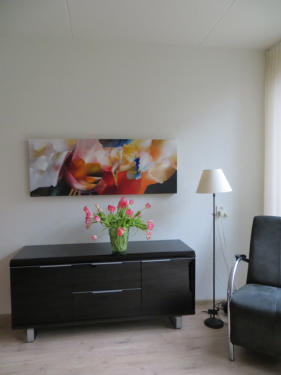 Olieverfschilderij met abstracte bloemen boven een kastje
